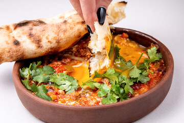 shakshuka with herbs, cheese and fresh pastries on a light background