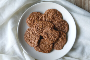 Plate of healthy, gluten free and high protein cookies, made with bananas, eggs, chia seeds and almonds. White tablecloth and wooden background. Flat lay.