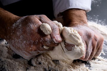 the chef kneads the dough on a dark background, the table is strewn with flour