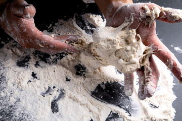 the chef kneads the dough on a dark background, the table is strewn with flour
