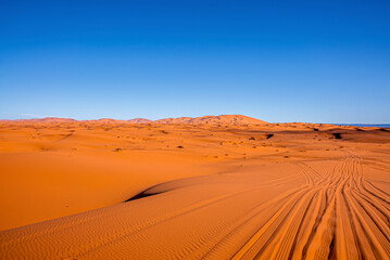 Fototapeta na wymiar Beautiful view of sand dunes with tyre marks in sahara desert against blue sky, Tyre marks on sand in desert