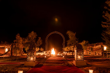 Glowing lanterns beside carpet on sand in sahara desert during night, Illuminated lanterns with ornamental pattern on sand - obrazy, fototapety, plakaty