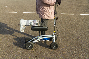 Woman with leg and foot  in surgical boot using a knee scooter walker landscape. - obrazy, fototapety, plakaty