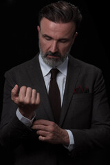 Portrait of a stylish elegant senior businessman with a beard and casual business clothes in photo studio adjusting suit