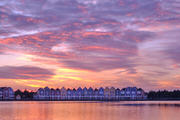 Purple skies and sunset over lake De Rietplas in Houten in the Netherlands. Row of colourful wooden newly built Dutch houses in the distance.