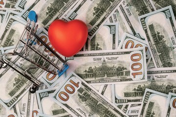Shopping cart and red heart on a background of one hundred dollar bills. Economics and finance