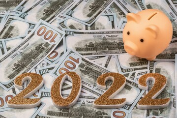 Golden numbers 2022 and a piggy bank against a background of one hundred dollar bills.