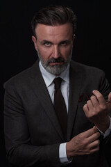 Portrait of a stylish elegant senior businessman with a beard and casual business clothes in photo studio adjusting suit