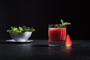 Un vaso de refrescante jugo de fresa triturado decorado con una rama de menta y fresas cortadas sobre un fondo negro   © R. Guas