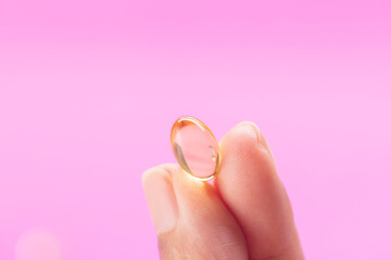 Hand Holding capsule of Omega 3 on pink background.
