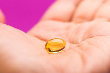 Hand Holding capsule of Omega 3 on pink background.