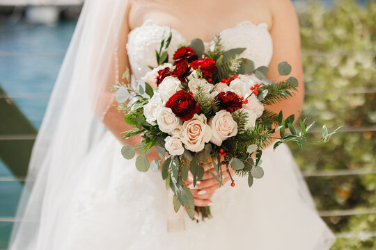 Beautiful wedding bouquet of flowers in hands of the  Bride holding an elegant bouquet made of white and red flowers and greenery Cropped photo	