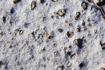 Schnee auf Forstweg mit Kies und Sonne, Hintergrund Steine
