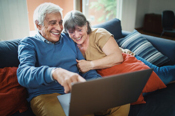 Senior couple watching funny content on a laptop sitting on the couch