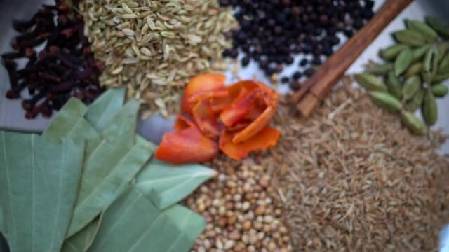 4k motion footage of Indian spices arranged in a traditional dish. Camera pans out and away from herbs and spices. Rack focus food video.
