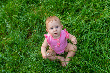 Naklejka na ściany i meble The child sits on the grass in summer. Selective focus.