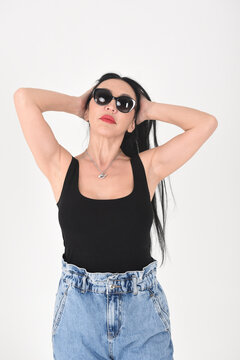 A gorgeous brunette in the studio on a white background in sunglasses corrects her hairstyle