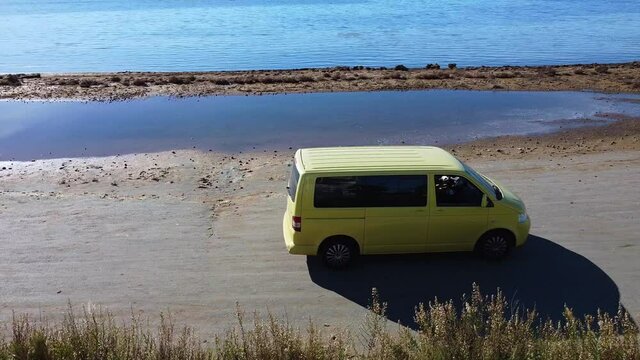 yellow camper van arrives at the beach in front of the sea during a summer trip - girl alone traveling goes down and looks at the sea - view from the drone in Murcia Spain Mar minor 