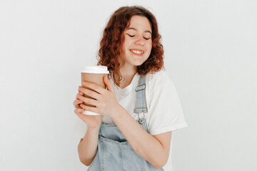 Smiling redhead girl with closed eyes, wearing denim dungarees and white t-shirt, glad to finish...