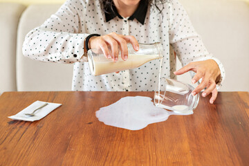 Mujer derrama el vaso de leche en la mesa - obrazy, fototapety, plakaty