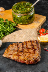 Grilled beef steak on a black board on a background of chimichurri sauce.