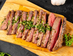 Sliced juicy medium roasted beef steak on a wooden board drizzled with chemichurri sauce top view.