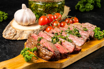 Steak chopped into pieces served on a wooden board on a background of tomatoes, garlic.
