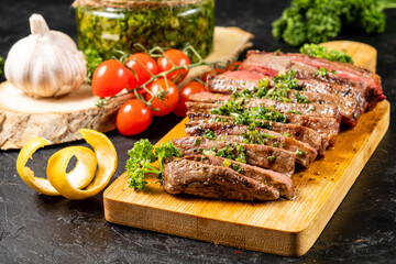 Medium rare steak sliced with homemade chimichurri sauce. Dark table. In the background, chenosque, cherry tomatoes.
