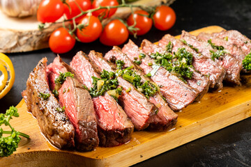 Juicy beef steak sliced and served on a wooden board and drizzled with fresh green chimichurri sauce. Close-up, selective focus.