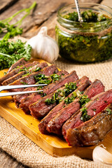 Appetizing pieces of steak with chimichurri sauce on a wooden table.