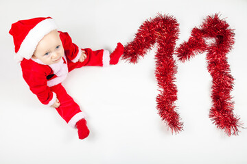 Smiling happy newborn infant eleven month baby in the red santa claus costume clothes with tinsel...