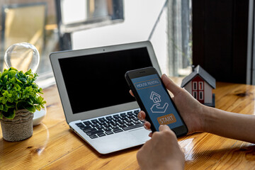 Person hold a smartphone in front of a rental home search website, using the smartphone to search for rental properties on the Internet. Using a smartphone to search for a house to rent online concept