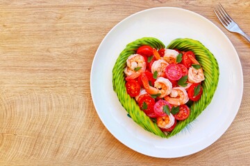 Heart shaped avocado with roasted shrimps,cherry tomatoes and parleys on plate with wooden background.Love healthy food concept for Valentine's day.Top view.Copy space