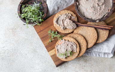 Homemade meat or chicken liver pate with multigrain crackers and microgreen, concrete background. Top view.