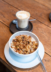 Breakfast with tasty oatmeal with caramelized apples and granola and glass of cappuccino on wooden...