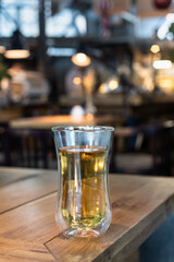 Glass cup with green or herbal tea on wooden table in cafe. Blurred interior background.