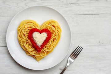 Heart shaped spaghetti with tomato sauce and parmesan cheeses on white plate with white wood background.Romantic vegetarian art food idea for Valentine's dinner.Top view.Copy space