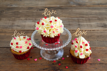 Three cupcakes with red topping decoration and a wooden sign with the word LOVE on a wooden background. Copy space.