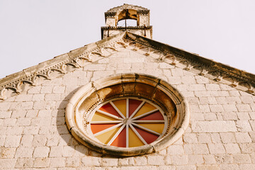 Rose window with multicolored glass on the stone wall of the church
