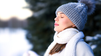 Side beauty portrait of beautiful attractive girl, young calm woman is breathing deep deeply fresh air at winter cold frosty snowy day with her eyes closed, meditating, doing breath exercise, enjoying - obrazy, fototapety, plakaty
