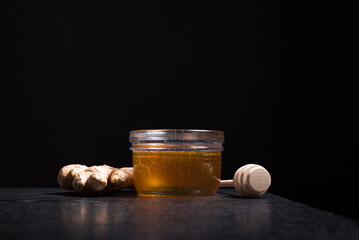 Miel de abeja en un frasco de vidrio con jengibre y un gotero de madera sobre fondo negro. Aislado