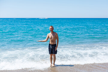 Attractive young man with a beautiful body in shorts walks along the sandy seashore and enjoying summer vacation