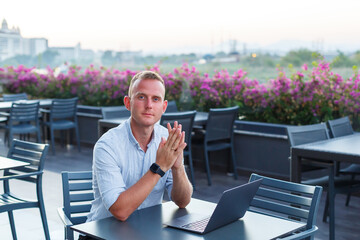 Successful young executive looking while sitting at a table with a laptop on a hotel terrace and...