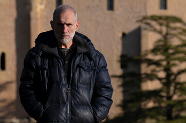 Portrait of adult man in winter clothes standing on hill with castle building on background. Segovia, Spain