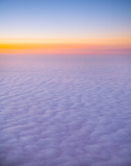 view of sea of clouds at sunset out of airplane window seat window orange sunset with pink and purple fluffy clouds as seen while in flight on airplane our of plane window heavenly horizontal format 