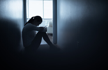 silhouette of a sad woman sitting next to window in a dark room 