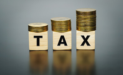 Tax concept with stacked gold coins on wooden blocks.  