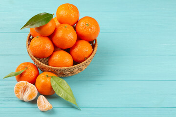 Fresh clementine mandarins or tangerines in a wooden bowl on blue background with copy space