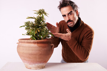 a young man pointing his finger at a cannabis plant on a white background