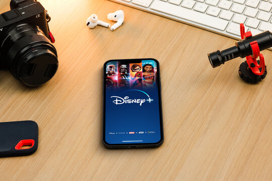 Disney+ (Disney Plus) app on smartphone iPhone 13 screen on wooden table. Content creator environment with keyboard, camera and mic. Rio de Janeiro, RJ, Brazil. December 2021